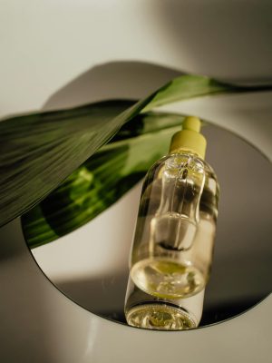 A stylish vertical shot of a cosmetic serum bottle with a leaf accent on a reflective surface.