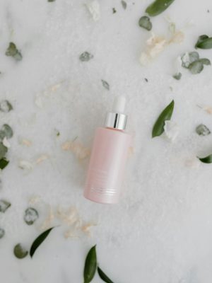 Minimalist shot of a pink dropper bottle for skincare against a marble background with scattered petals.