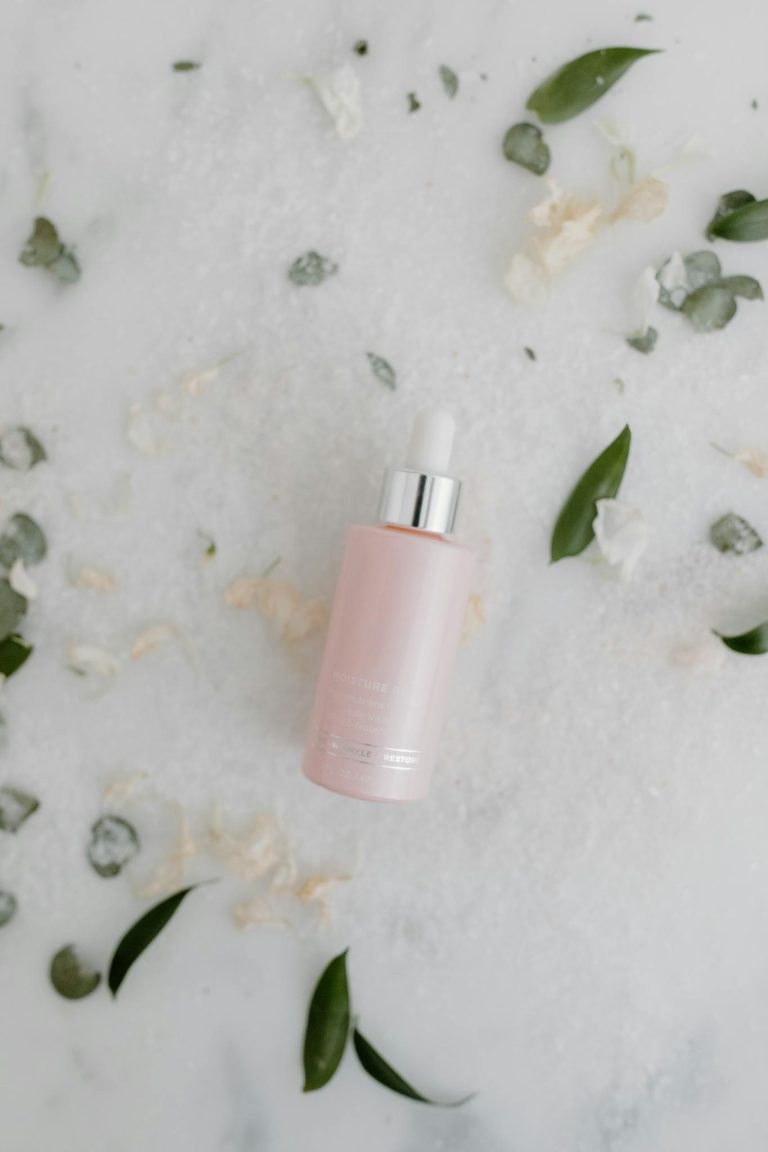 Minimalist shot of a pink dropper bottle for skincare against a marble background with scattered petals.